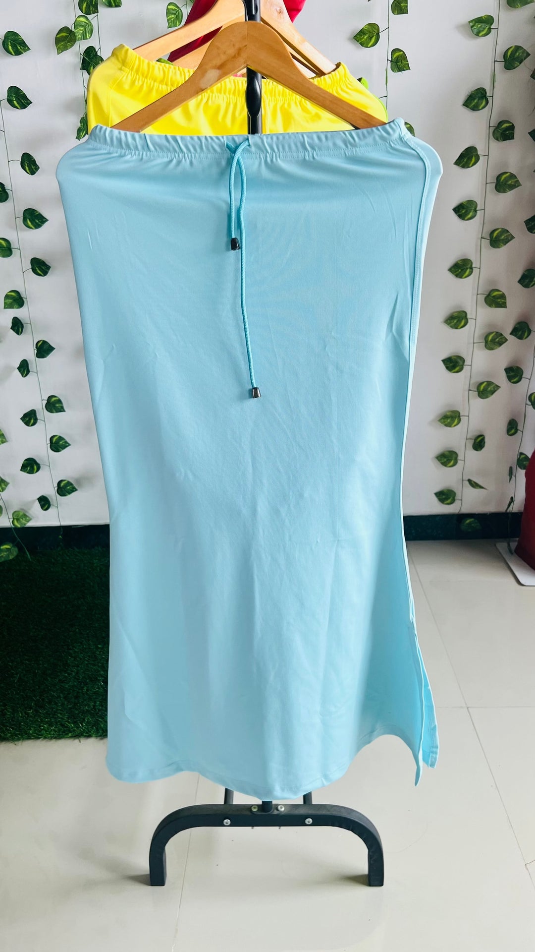 Sky blue stretchable sareeshaper with drawstring waist hanging on a wooden hanger against a leafy background