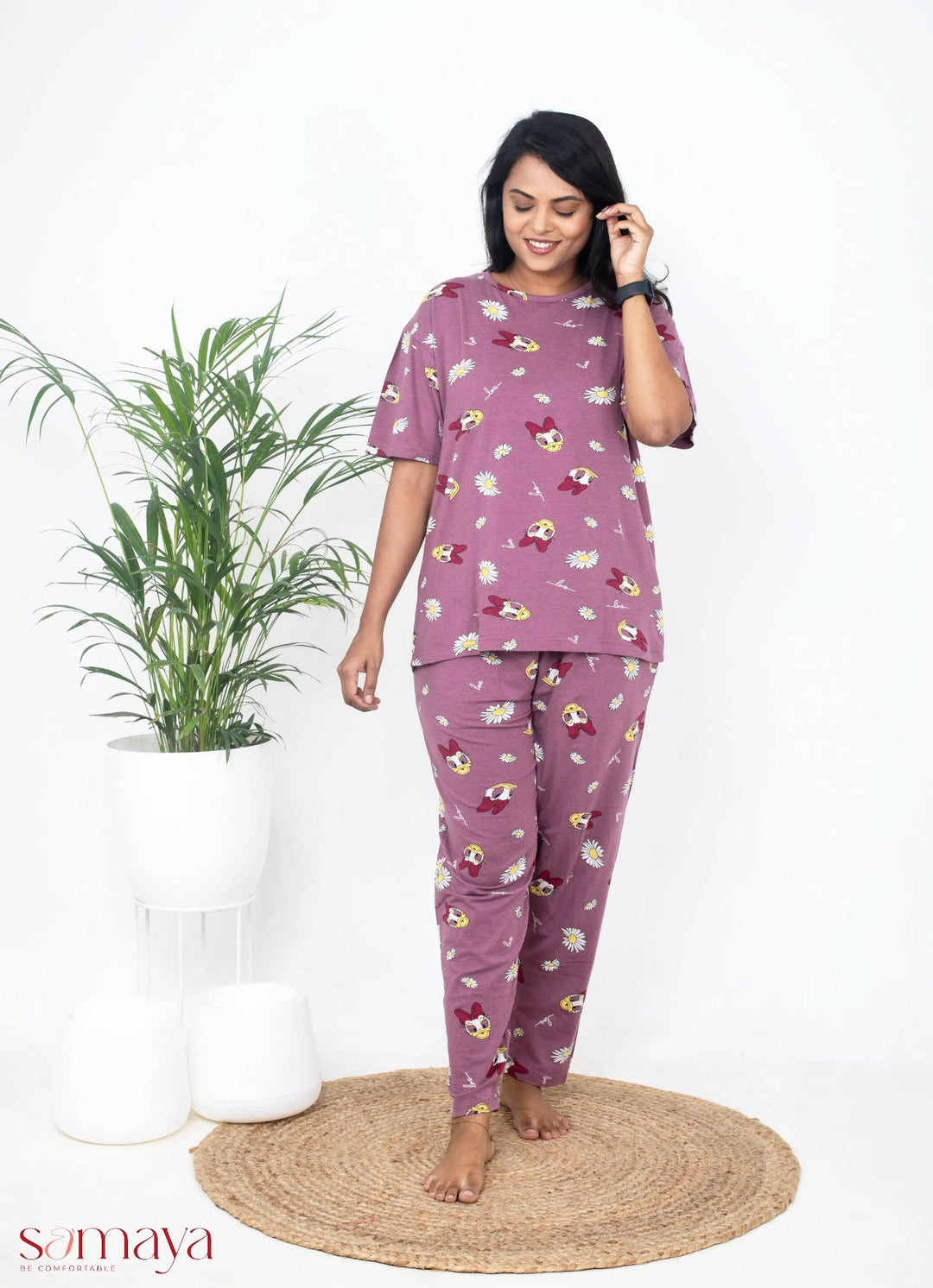 Woman wearing mauve cotton relaxed fit Mauve Donald Pant Set with cartoon prints, standing barefoot on a round woven rug next to a potted plant
