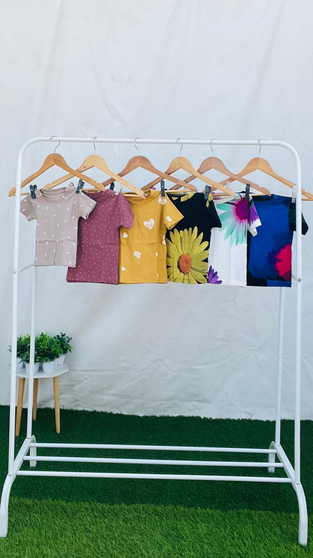 Pack of 5 unisex baby t-shirts in various colors and patterns on wooden hangers displayed on a white rack.