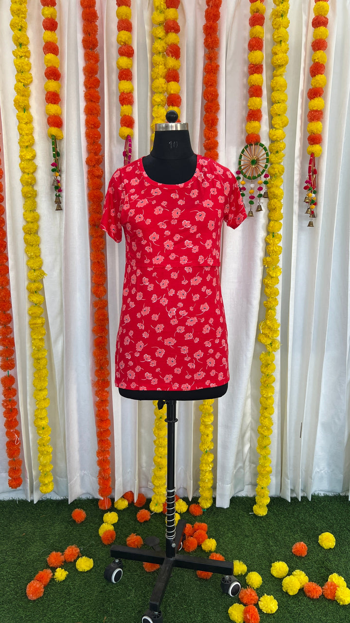 Red scarlet lightweight maternity t-shirt with floral print, oversized relaxed fit, side slits, and nursing flaps on mannequin against marigold flower backdrop