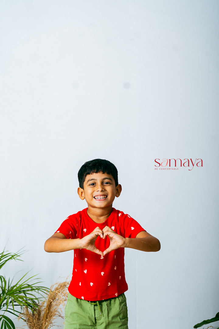 Unisex red baby t-shirt with white heart prints, round neck and short sleeves made of 95% cotton and 5% lycra ribbed fabric.