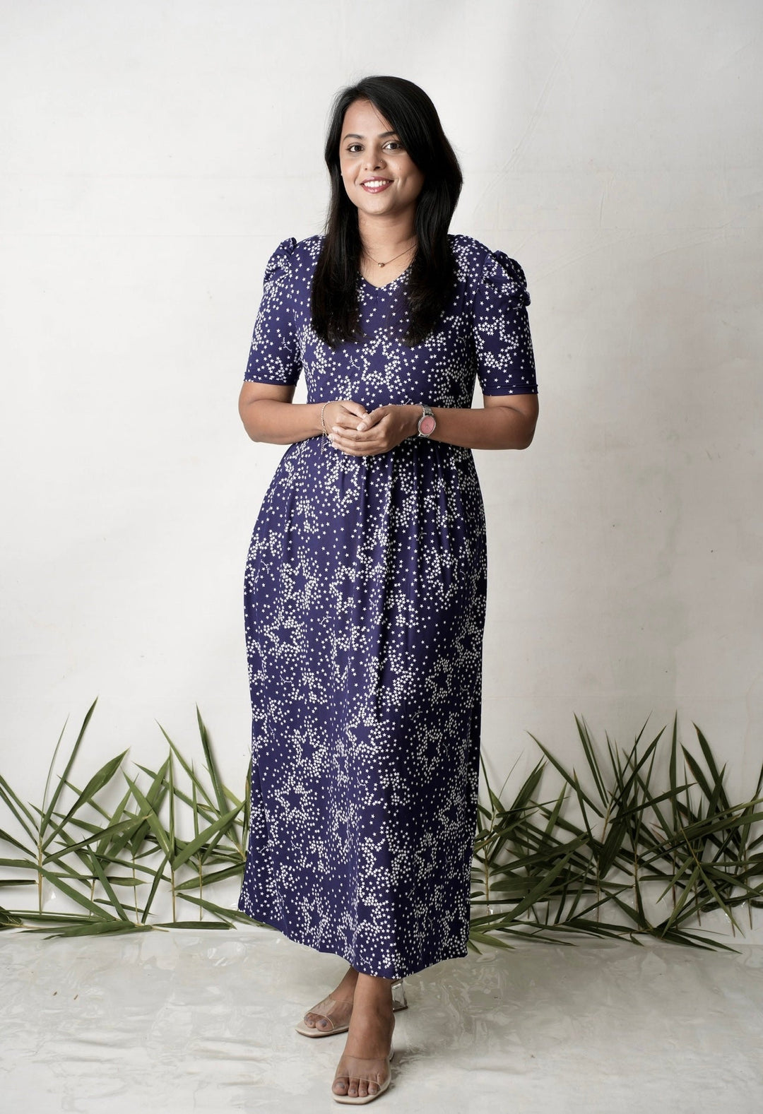 Woman wearing a purple floral maxi stardust light weight nursing dress with elbow puff sleeves and V-neckline standing indoors