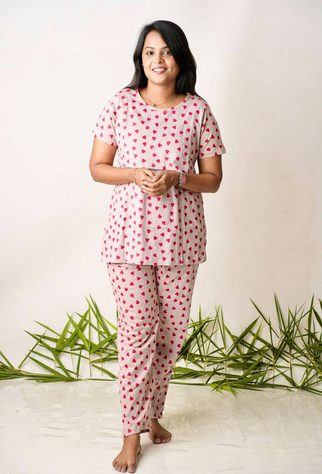 Woman wearing red heart print maternity feeding pant set with short sleeves and round neckline, standing barefoot indoors