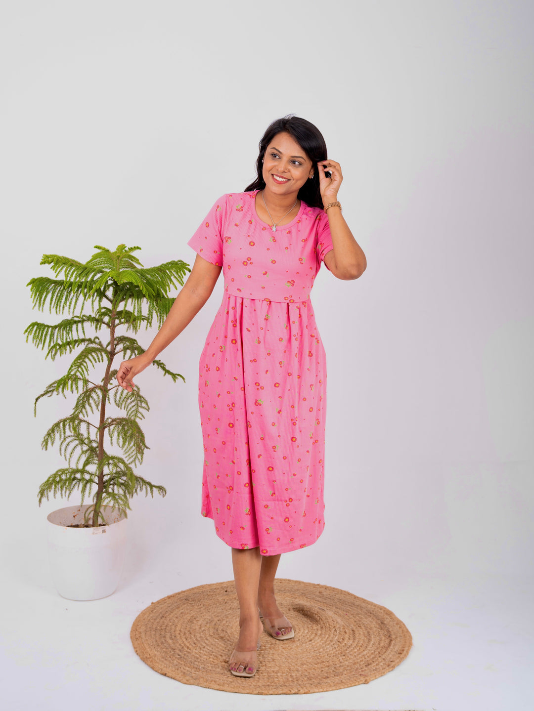 Woman wearing pink Midi Rosey Ribbed Dress with flower print and short sleeves standing near a potted plant