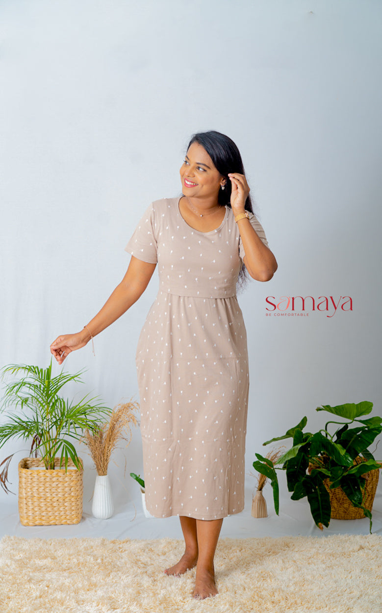 Woman wearing a beige midi creamy ribbed nursing dress with short sleeves and floral print standing indoors next to potted plants