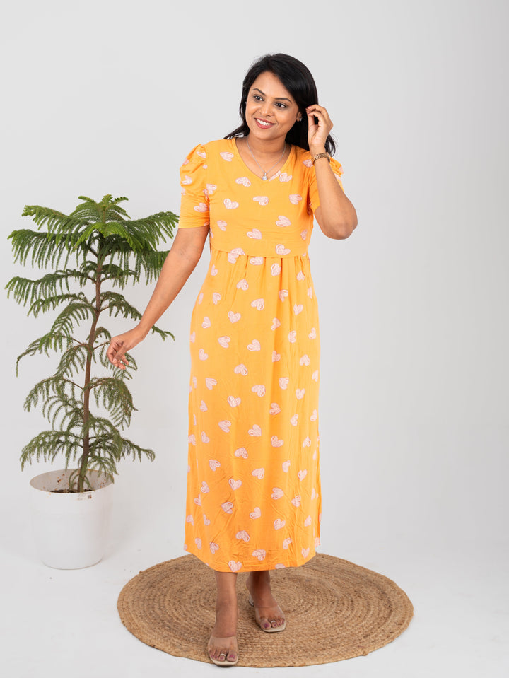 Woman wearing orange midi nursing gown with heart print and short sleeves standing indoors