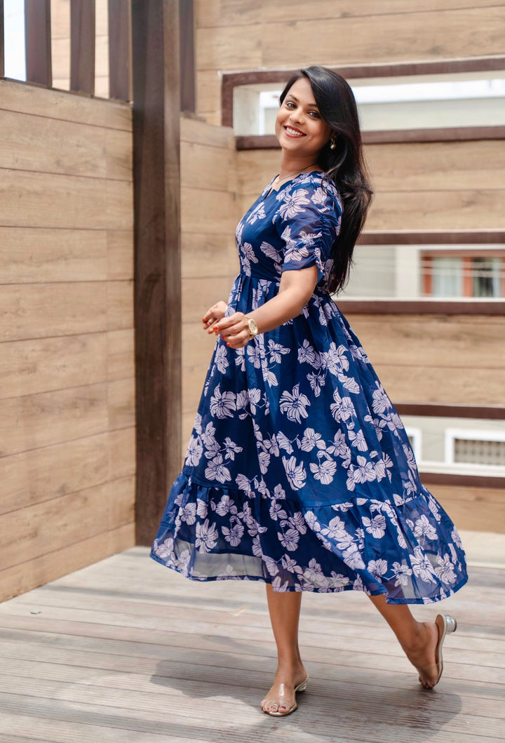 Smiling woman wearing blue floral Lilly Georgette casual calf-length dress with lining and fish cut sleeves, standing indoors