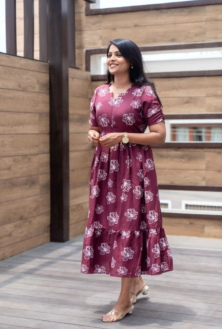 Woman wearing a maroon casual floral print dress with lining and center zip, standing outdoors on a wooden deck.