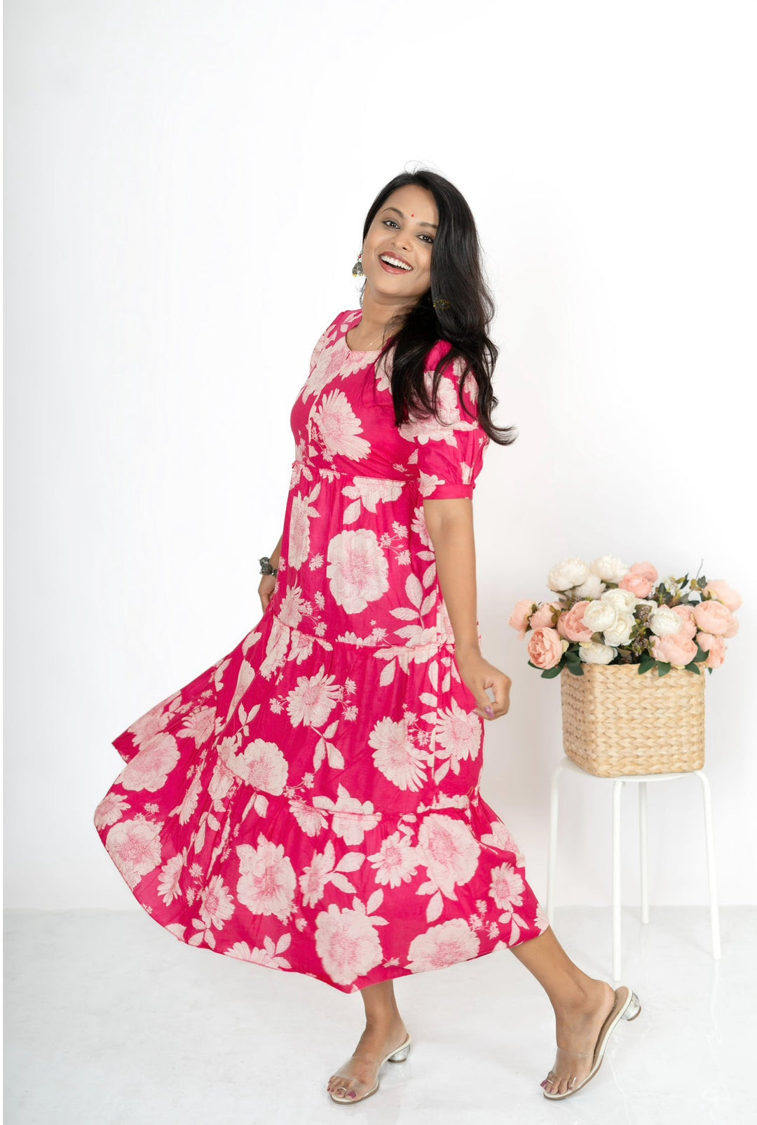Woman wearing pink sunflower day to night dress with elbow sleeves and center zipper, standing next to a basket of flowers