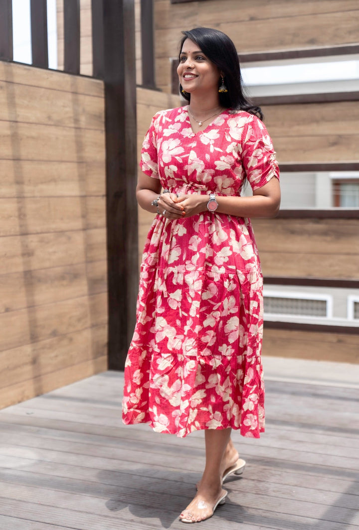 Woman wearing pink kantha casual dress with floral print and V-neck, standing outdoors on wooden deck