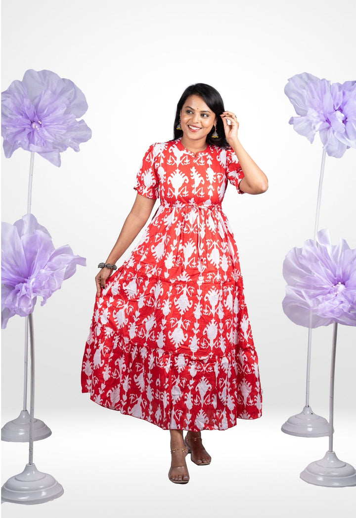 Woman wearing red and white floral Raga casual cotton maxi dress with puff sleeves and collar neck standing between purple flower decorations