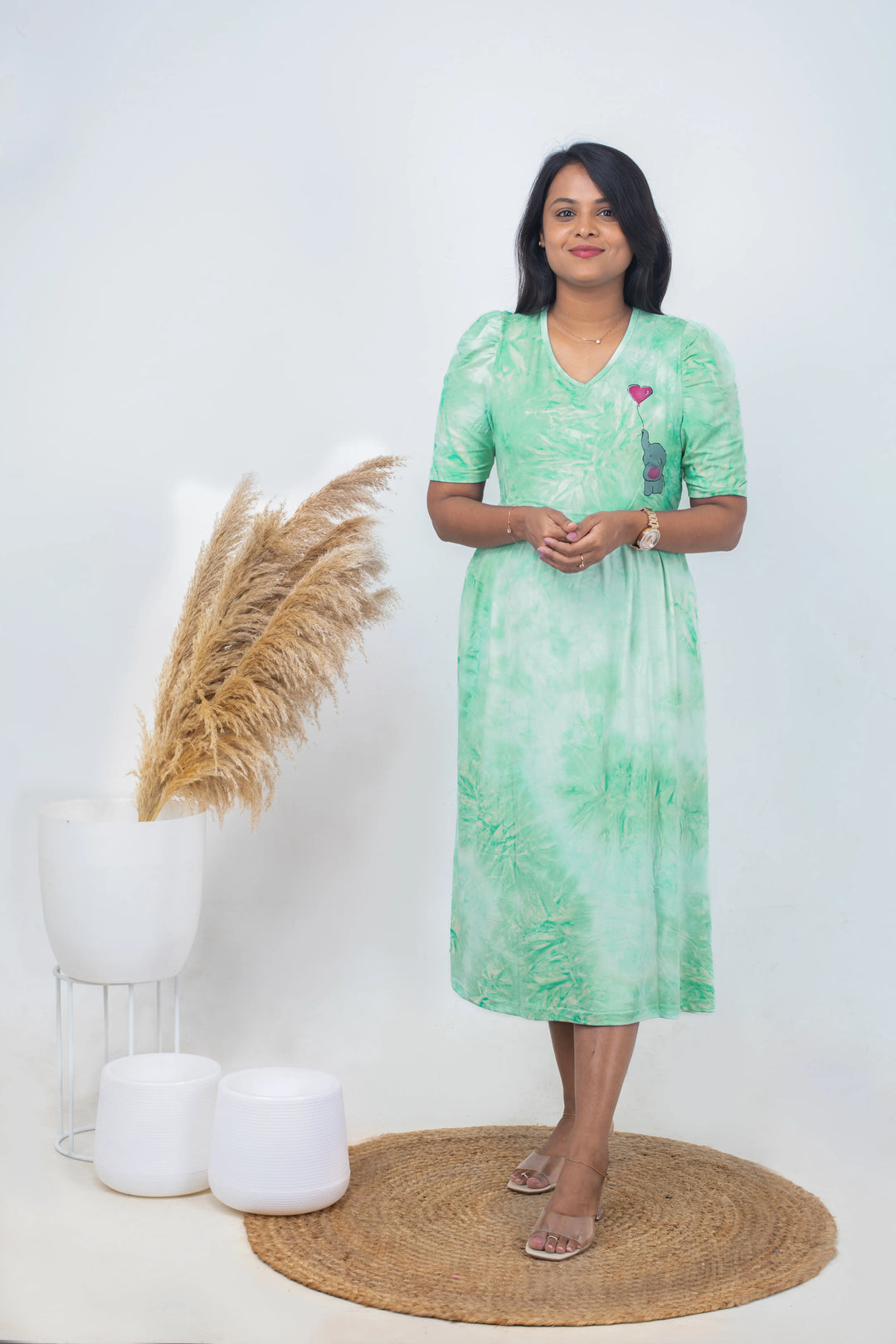 Woman wearing luxury midi crystal light green maternity nursing dress with puff sleeves and V-neck, standing indoors near decorative plants