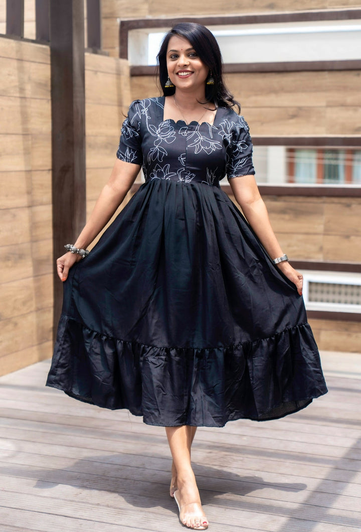Woman wearing black Maya Casual Dress with floral print, center zipper, and fish cut sleeves standing outdoors