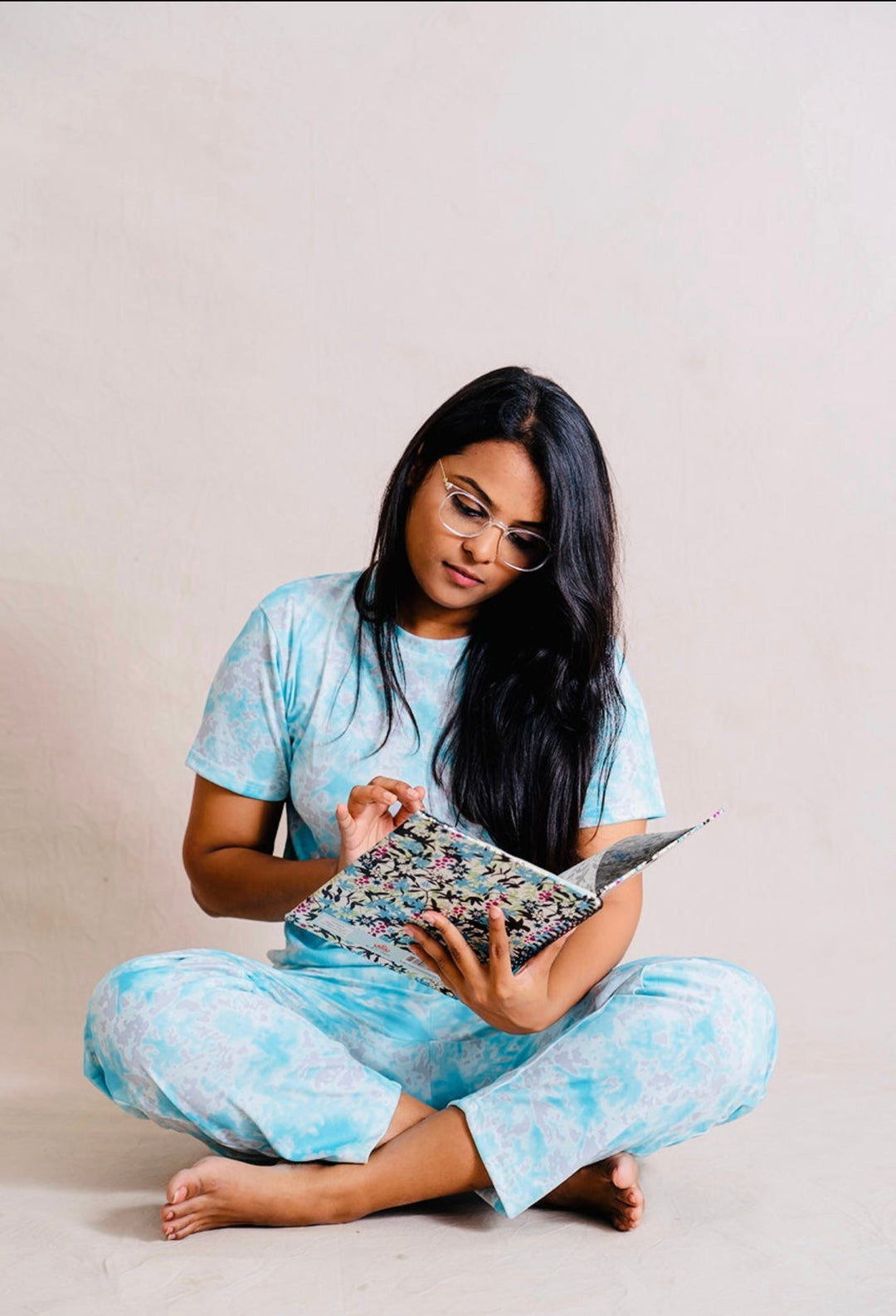 Woman wearing aqua feeding top and pant set sitting cross-legged reading a book