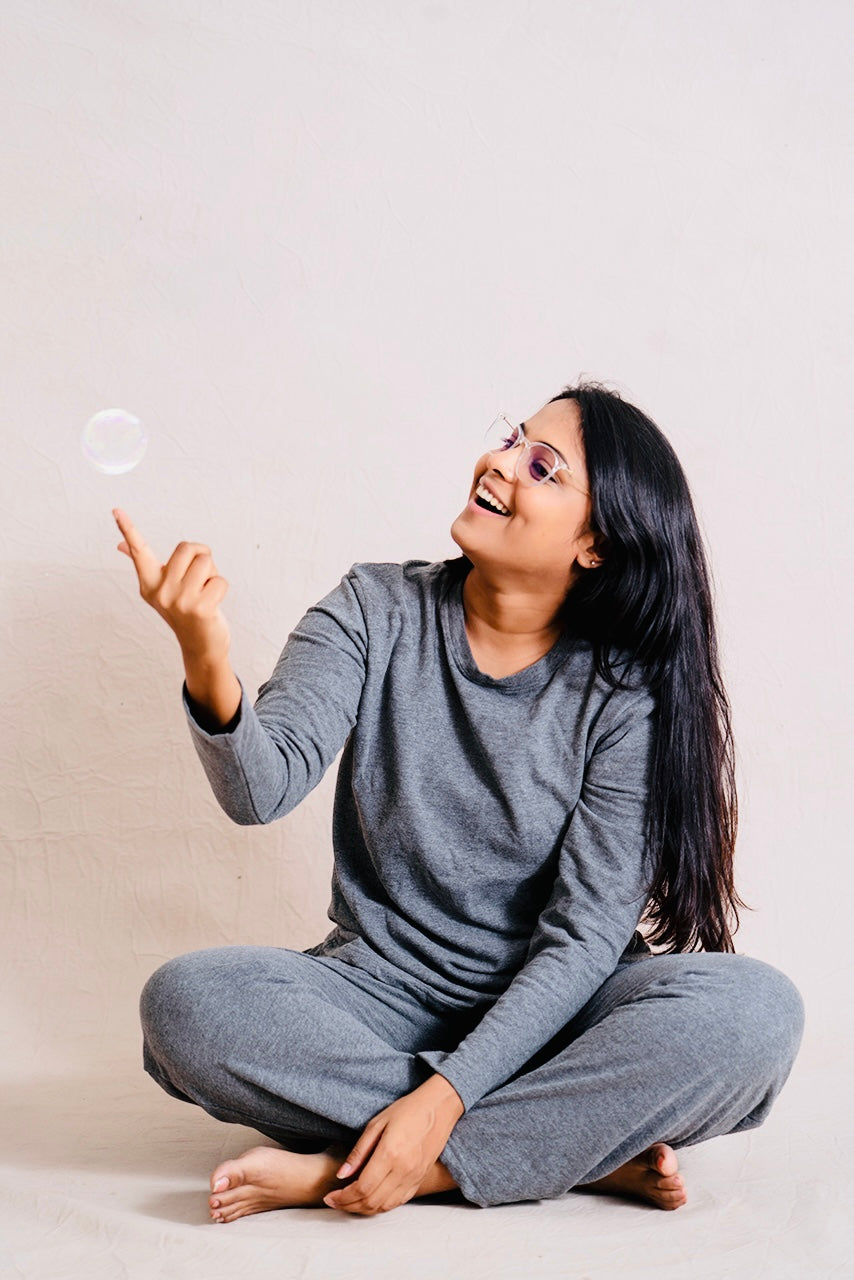 Woman wearing gray Twilight Pant Set loungewear sitting barefoot and playing with a bubble
